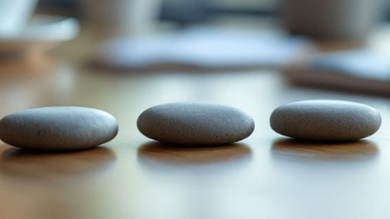 Smooth unmarked stones on a warm wooden tabletop, arranged in a steady path to symbolize consultation reminders